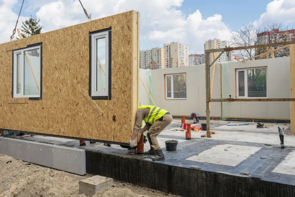 Worker in yellow construction vest working on modular home under construction.